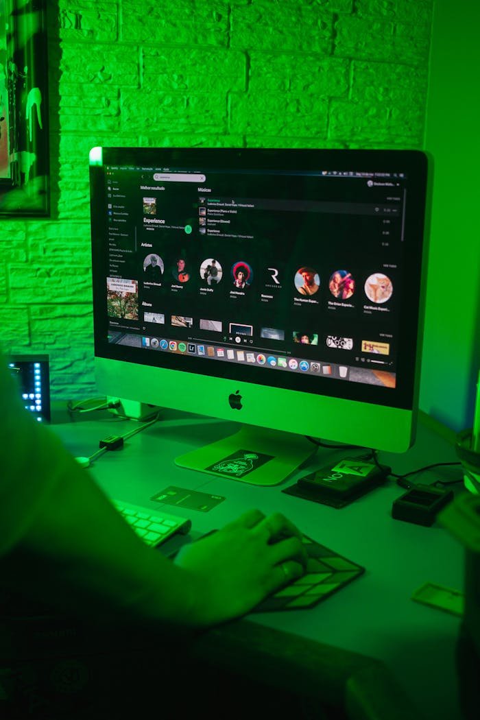 A desktop computer setup with green ambient lighting and a hand operating the mouse.